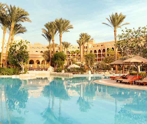 Utendørsbasseng med palmer og hotellbygning i bakgrunnen. (AI-generert tekst)