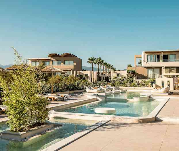 En luksuriøs resort med basseng, solsenger og moderne bygninger under en klar himmel. (AI-generert tekst)