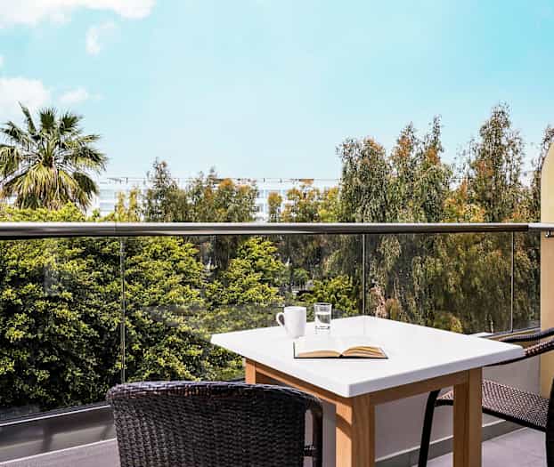 Bilde av en terrasse med et bord og to stoler, med utsikt over trær og en blå himmel. (AI-generert tekst)