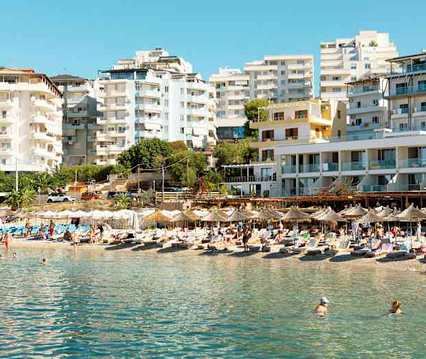 En strand med parasoller og solsenger foran høyhus. (AI-generert tekst)