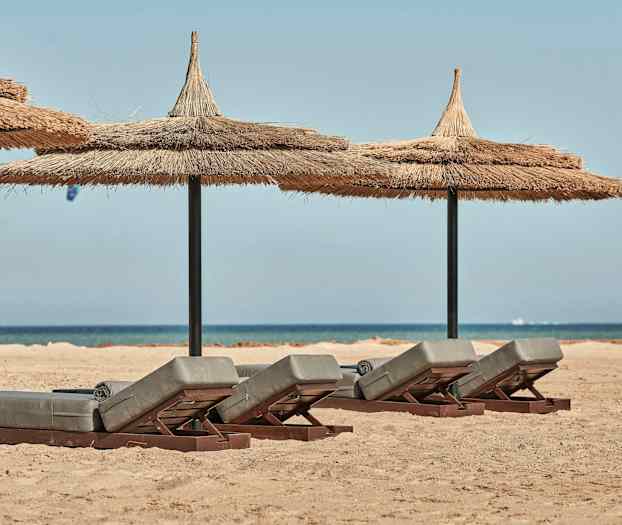 Solstoler med stråtak på sandstrand med hav i bakgrunnen. (AI-generert tekst)