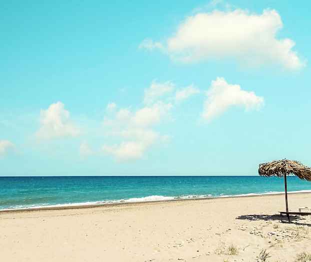 En sandstrand med parasoll, havet i bakgrunnen. (AI-generert tekst)