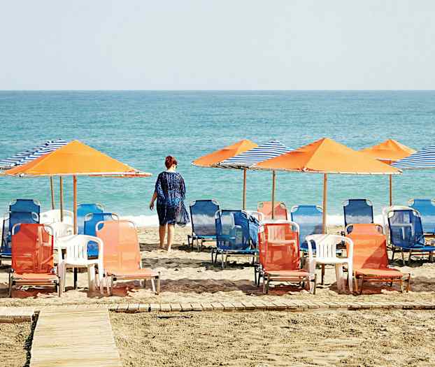 Strand med solsenger og parasoller, en person går mot havet. (AI-generert tekst)