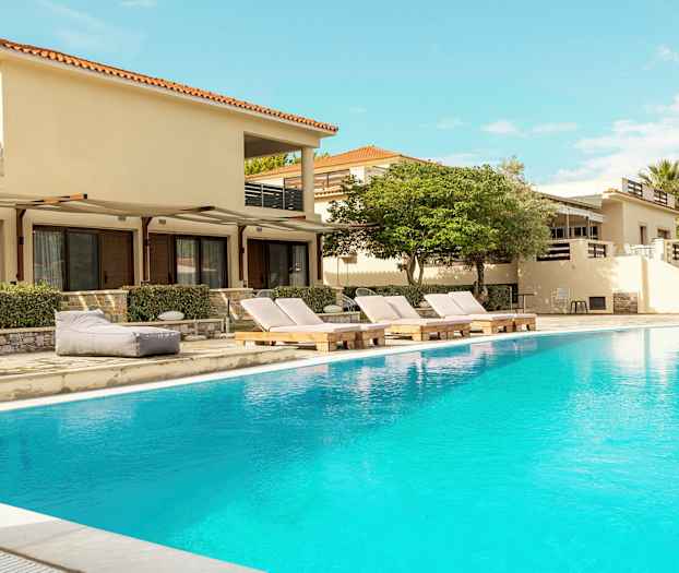 Utendørs svømmebasseng foran bygninger med solsenger og omgivende vegetasjon. (AI-generert tekst)