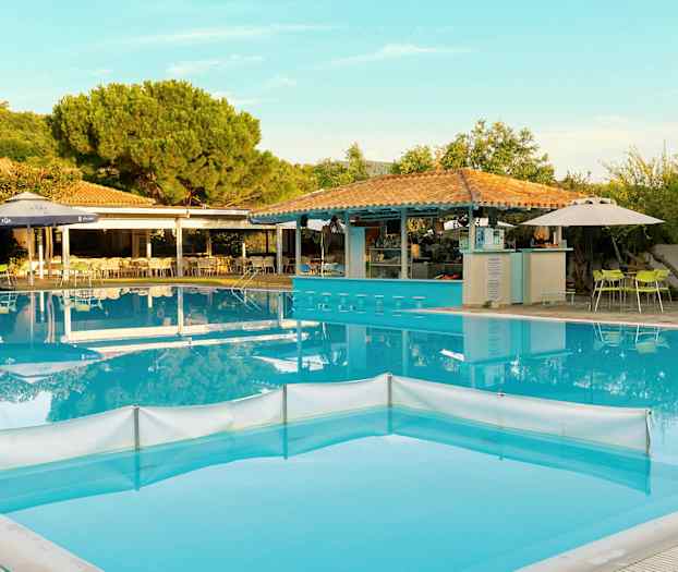 Et utendørs svømmebasseng med barkrakker i vannet, omgitt av bord og stoler samt grøntområder. (AI-generert tekst)