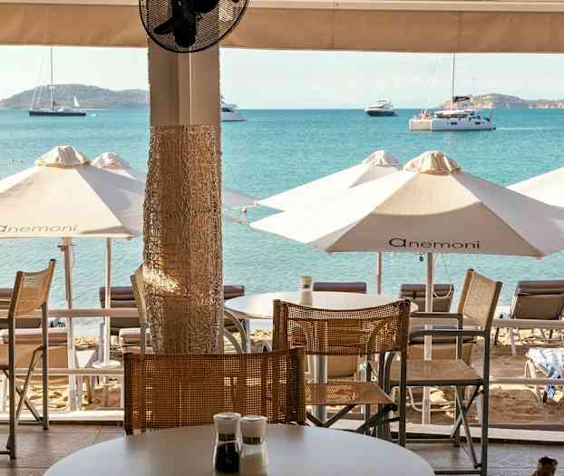 Utsikt fra en terrasse mot stranden med solsenger, parasoller og havet i bakgrunnen. (AI-generert tekst)
