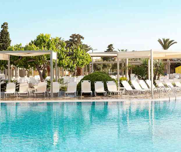 Et basseng med solsenger og skyggende paviljonger i bakgrunnen. (AI-generert tekst)