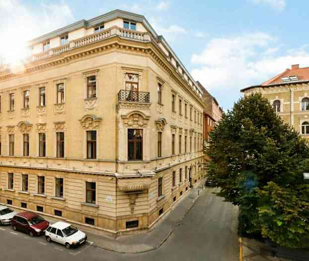 Gatelyktene står ved et grønt område omgitt av høye bygninger. (AI-generert tekst)