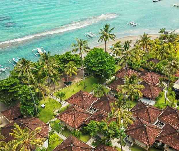 Luftfotografi av et strandferiested med røde hustak, omgitt av palmer og nær et turkis hav. (AI-generert tekst)