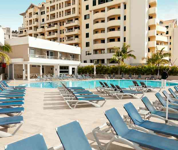 Utendørsbasseng med solsenger og omkringliggende bygninger. (AI-generert tekst)