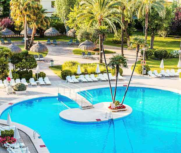 Et svømmebasseng omgitt av solsenger og parasoller, med palmer og grønn vegetasjon i bakgrunnen. (AI-generert tekst)