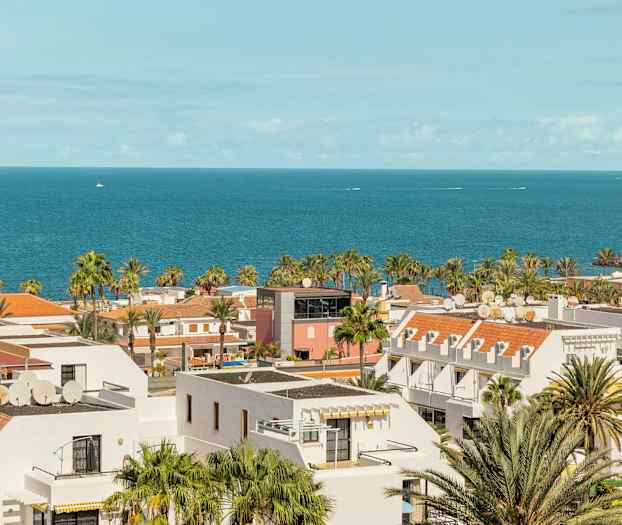 Utsikt over kystby med hvite bygninger, palmer og havet i bakgrunnen. (AI-generert tekst)