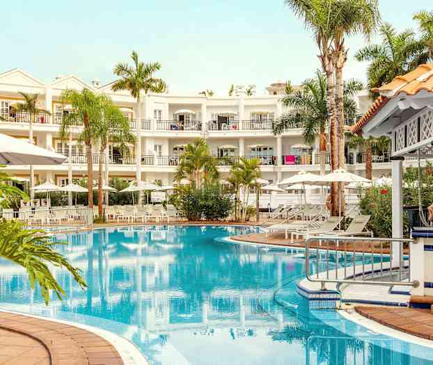 Bilde av et hotell med et basseng, omgitt av solsenger, parasoller og grøntområder. (AI-generert tekst)