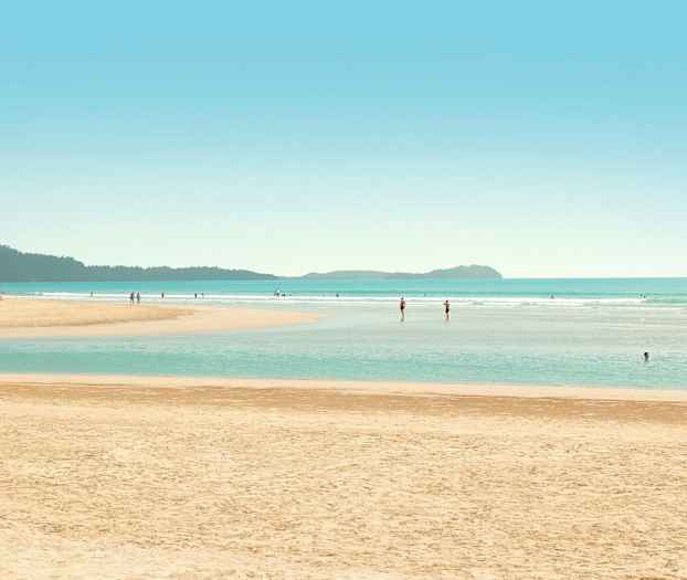 En strand med mennesker som svømmer og går i vannet. (AI-generert tekst)