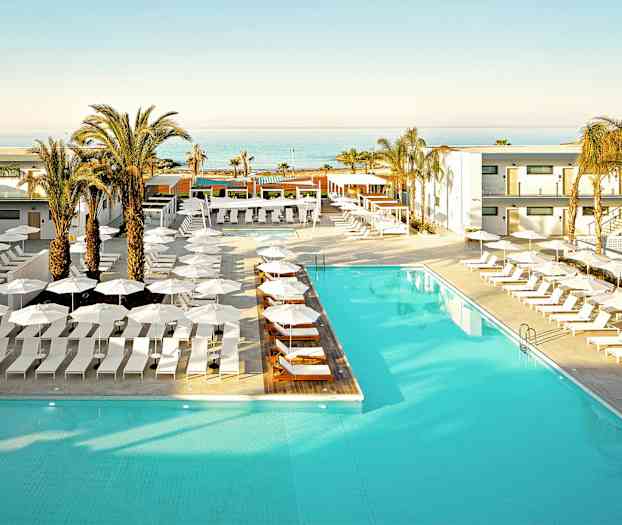 Et hotellbasseng omgitt av solsenger og parasoller, med palmer og en havutsikt i bakgrunnen. (AI-generert tekst)