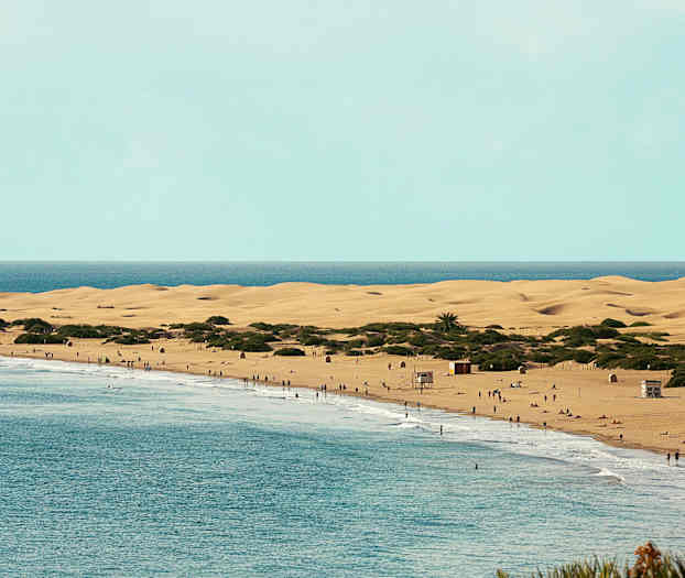 En strand med sanddyner og folk ved vannet. (AI-generert tekst)