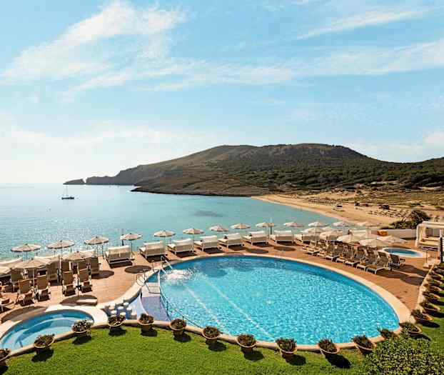 Bassengområde med solsenger og parasoller med utsikt over en strand og havet. (AI-generert tekst)