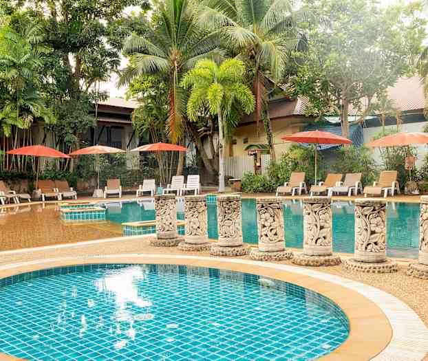 Et utendørs svømmebasseng omgitt av palmer og solsenger med parasoller. (AI-generert tekst)