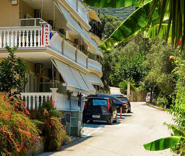 En bygning med balkonger og markiser ved en vei med parkerte biler og grøntområder. (AI-generert tekst)