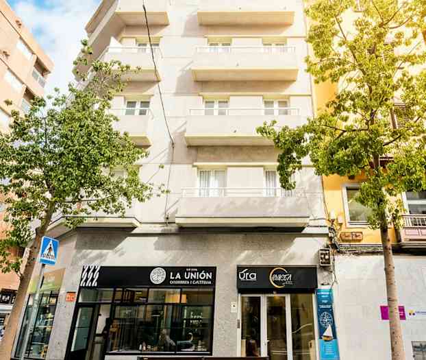 Boligbygg med balkonger, butikslokaler i første etasje og litt grøntområder rundt. (AI-generert tekst)