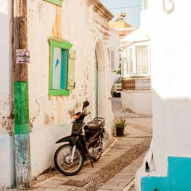 En moped står parkert mellom hvitkalkede småhus i en trang gate.