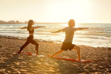 Mann og kvinne gjør yoga på stranden i soloppgangen