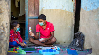 Voksen mann, fra Redd Barna, spiller kortspill med en ung gutt.