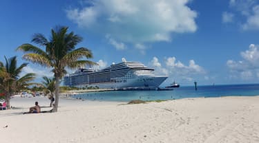 Cruiseskip ved hvit sandstrand med palmer.