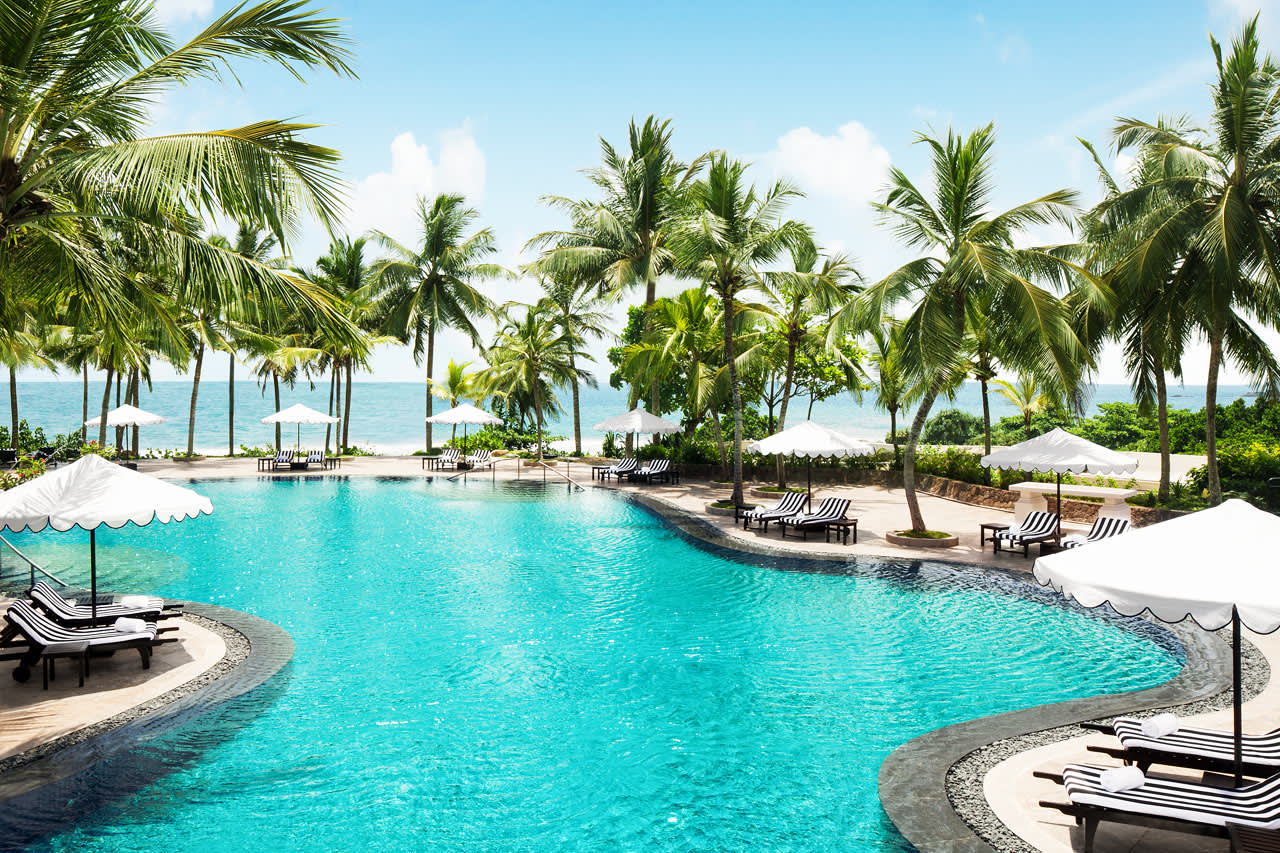 Ved hotellets koselige bassengområde skimter man havet mellom palmene