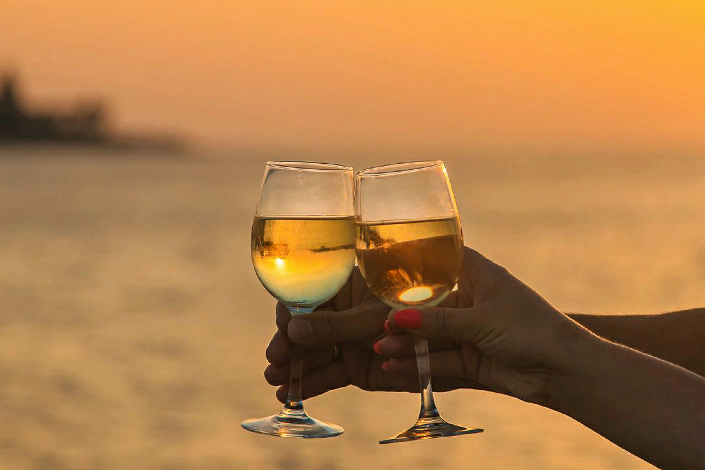 To vinglass skåler foran en solnedgang ved havet. (AI-generert tekst)