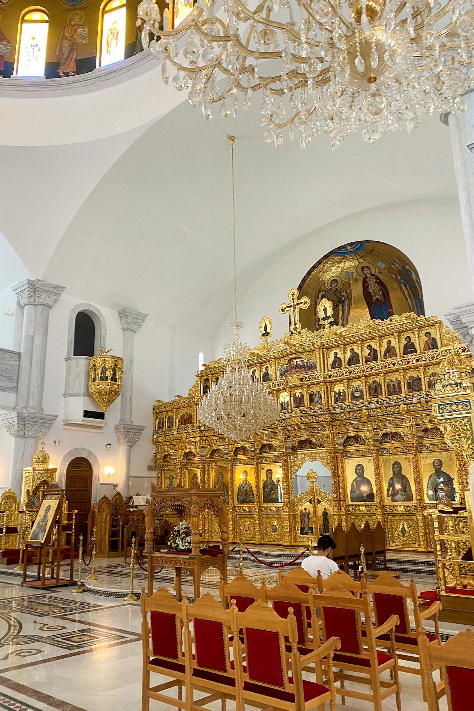 Et interiørbilde av en kirke med en gylden ikonostas, ikoner og en hengende krystalllysekrone. (AI-generert tekst)