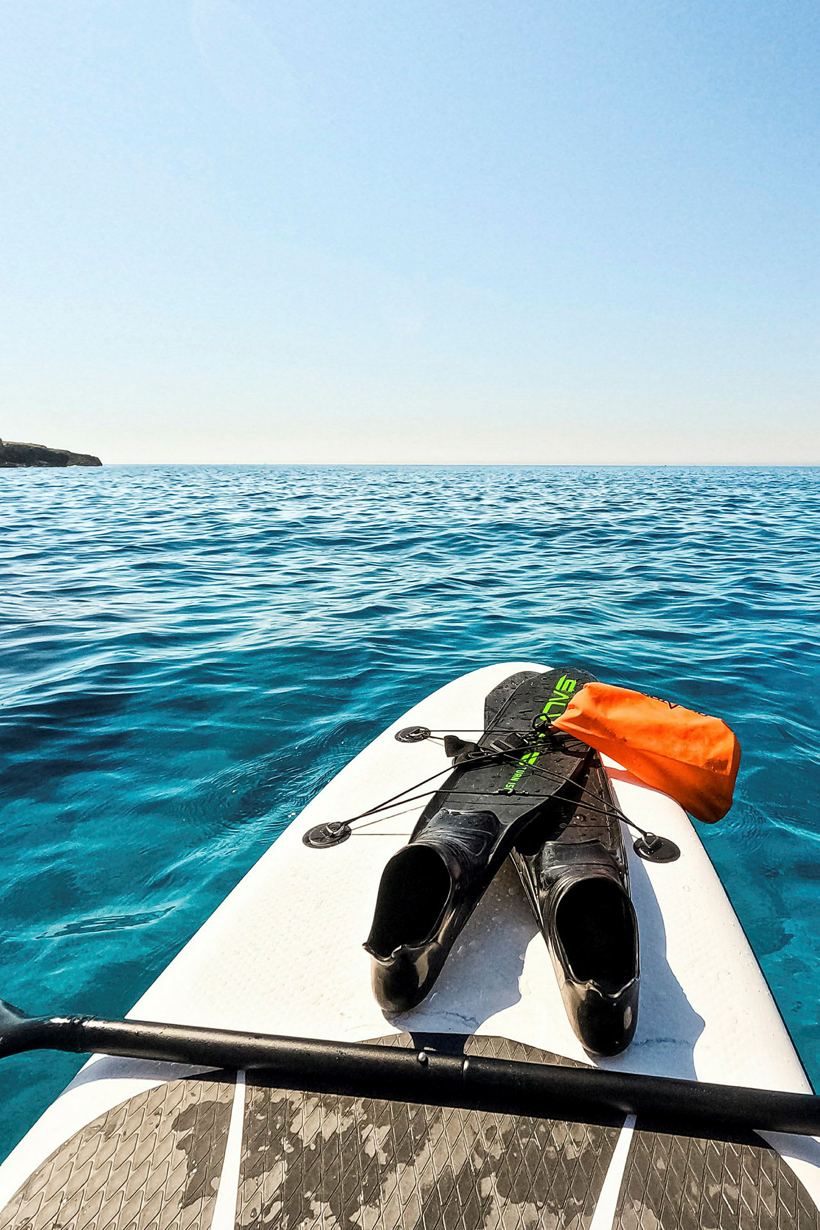 Et paddleboard med svømmeføtter og en oransje vanntett pose fotografert på et rolig hav. (AI-generert tekst)