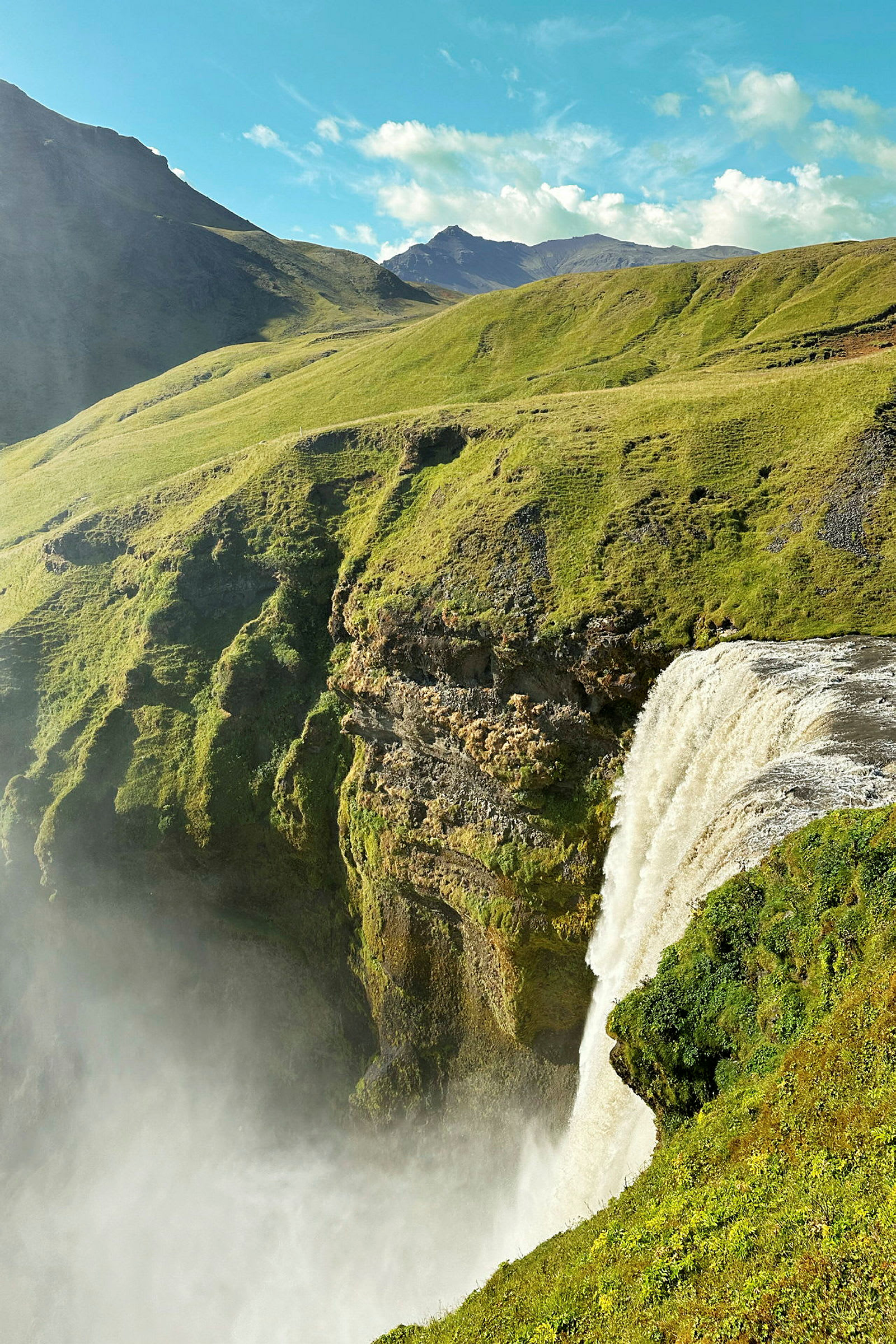 Et fossefall som renner over en frodig klippe i et fjellandskap. (AI-generert tekst)