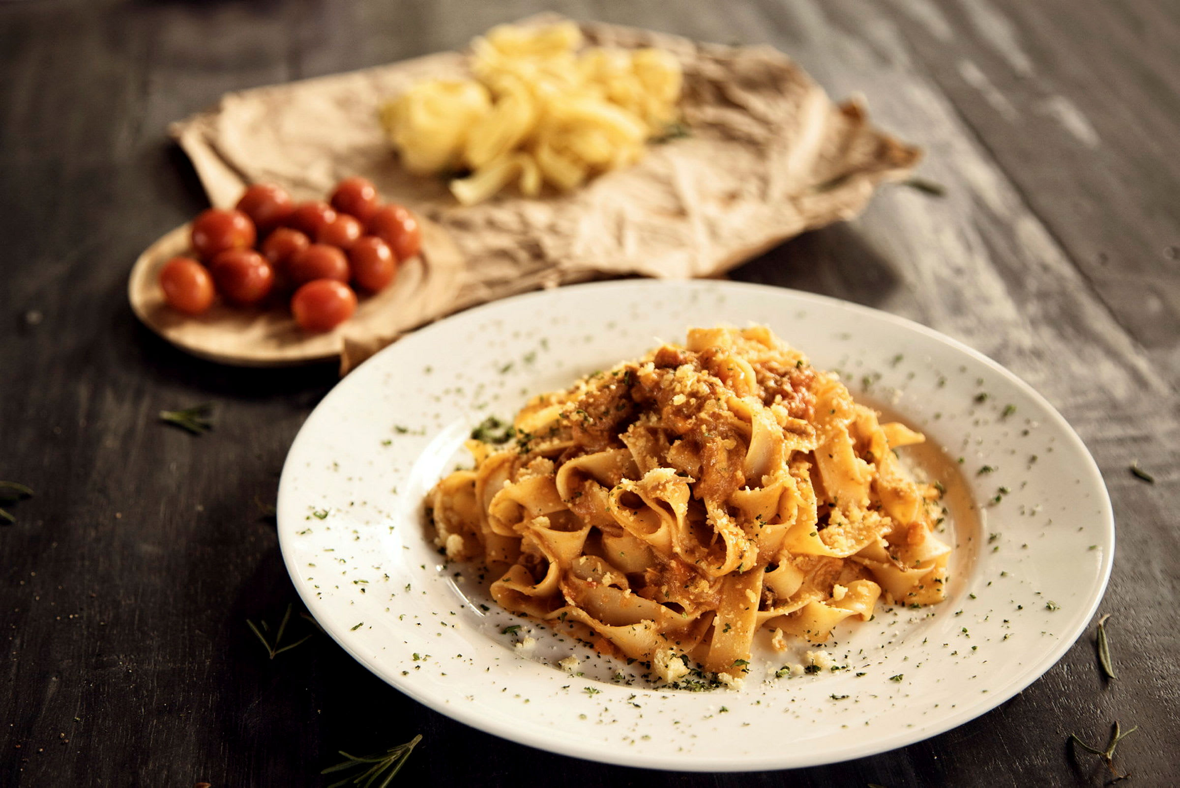 En tallerken med pasta toppet med saus og urter, med cherrytomater og rå pasta i bakgrunnen. (AI-generert tekst)