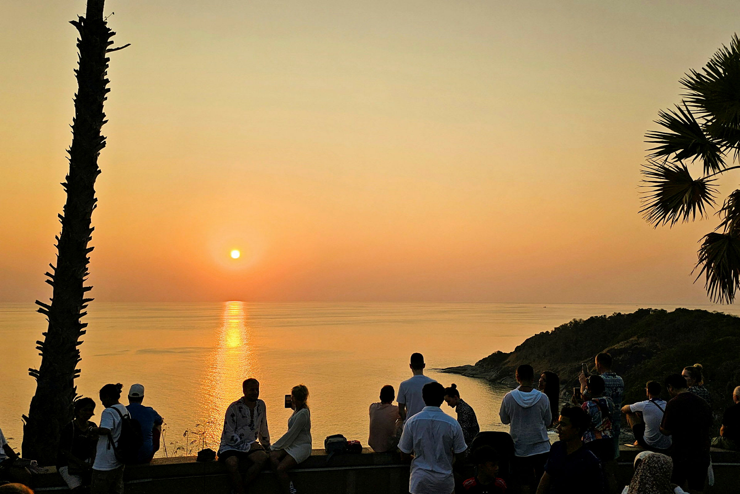 Solnedgang over havet med mennesker samlet på en utsiktsplass. (AI-generert tekst)