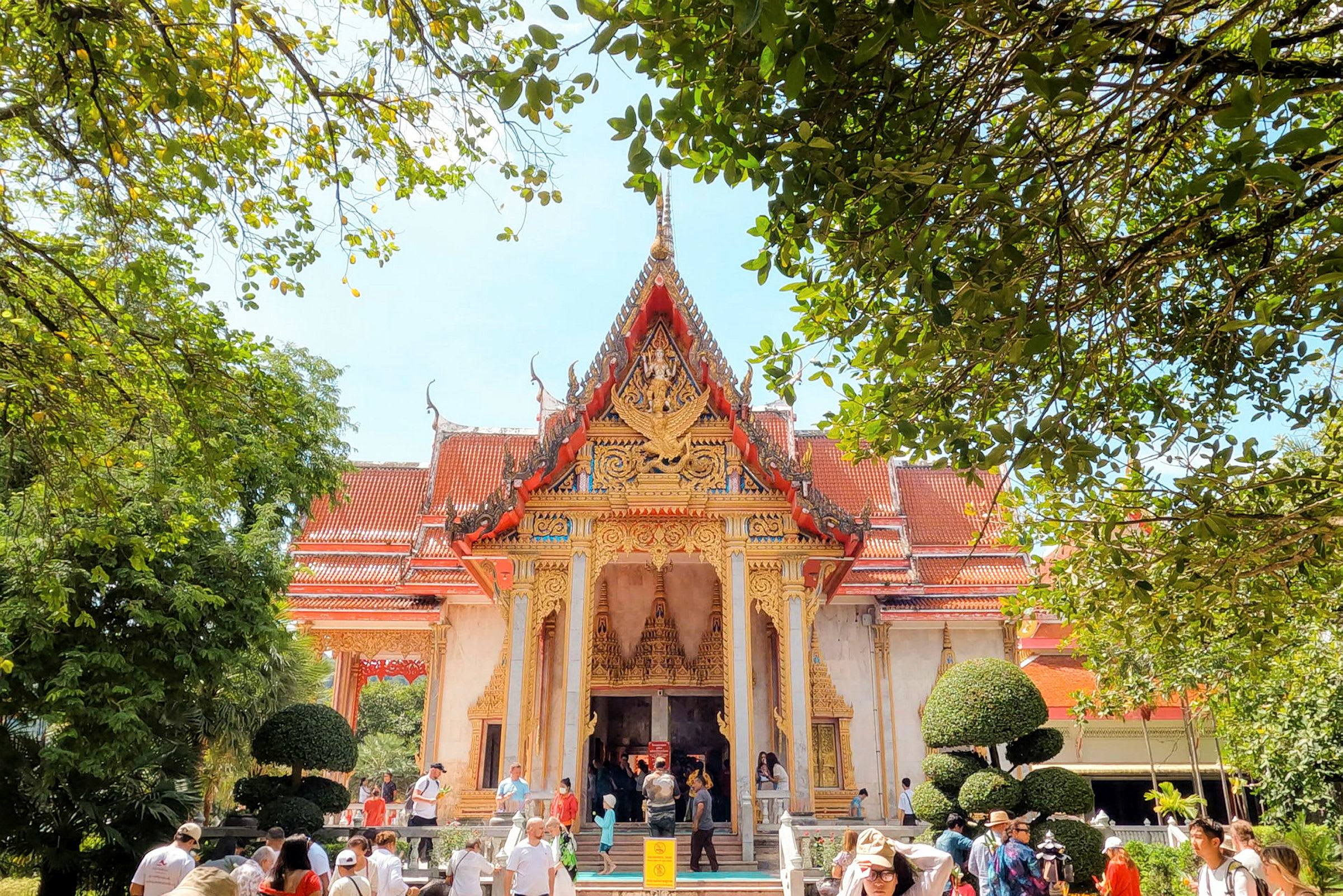 Bilde av et detaljrikt thailandsk tempel omgitt av frodig vegetasjon, med besøkende foran bygningen. (AI-generert tekst)