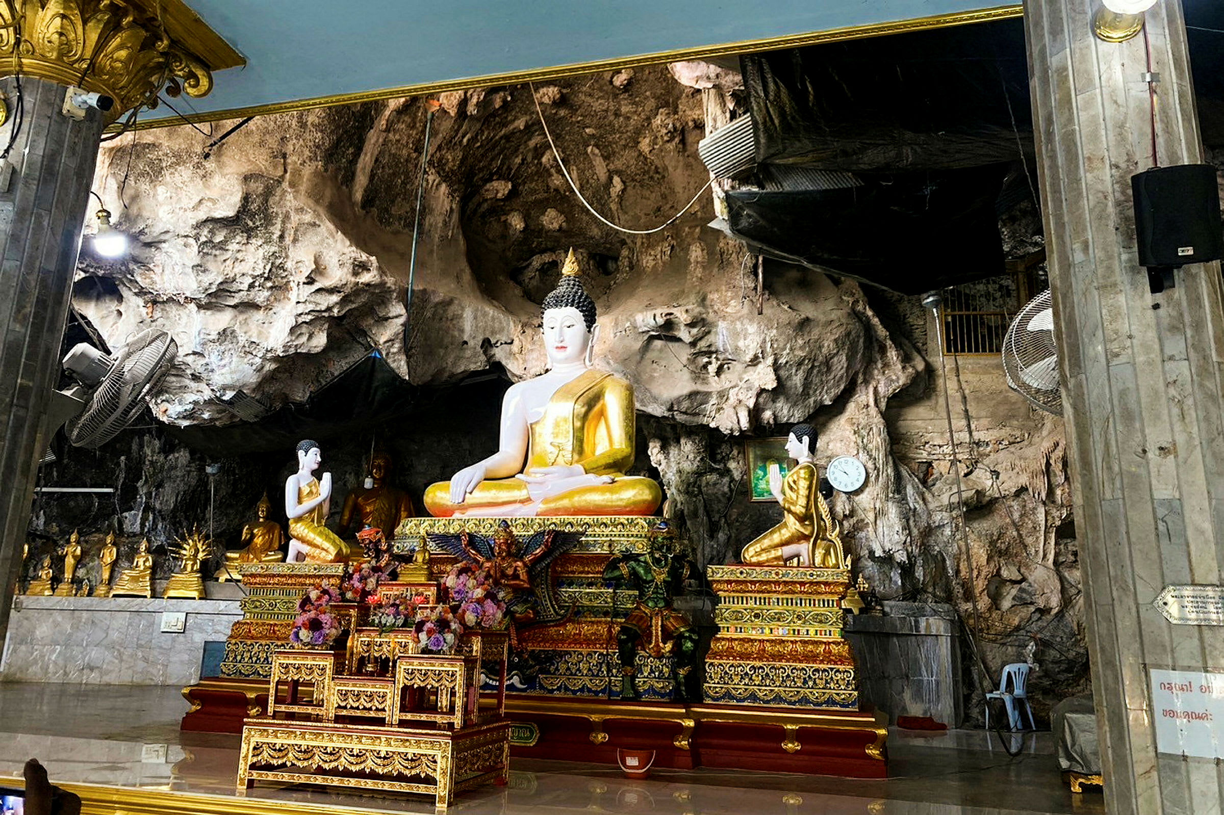 Bildet viser en buddhastatue i et dekorert miljø med klippevegger. (AI-generert tekst)