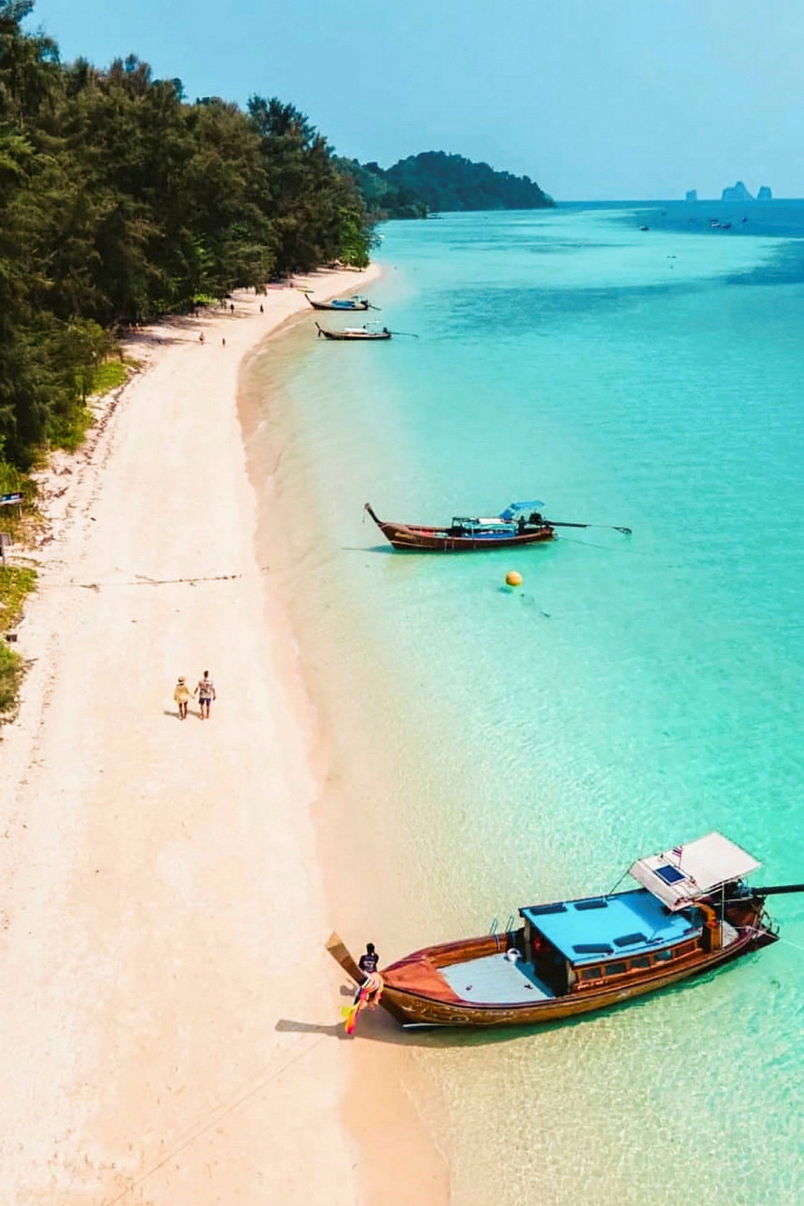 Bildet viser en gyllen strand med klart turkis vann og trebåter nær stranden. (AI-generert tekst)