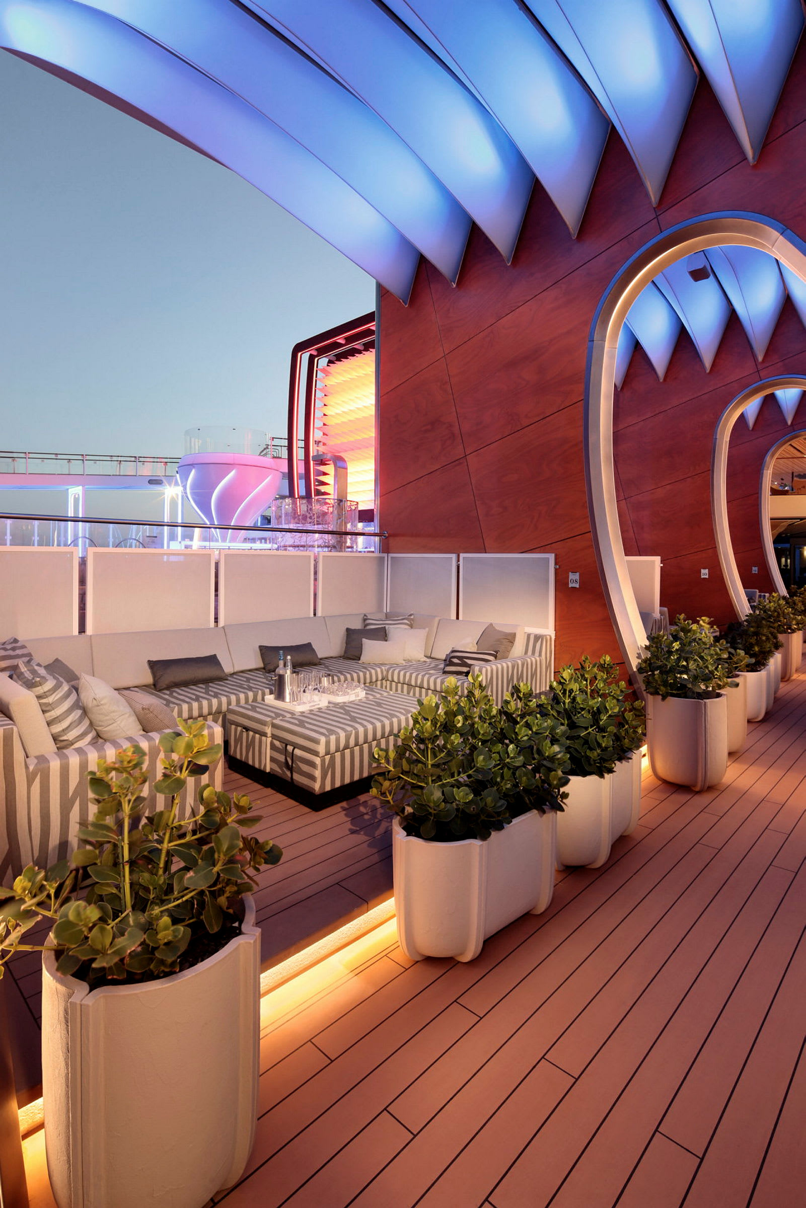 En moderne lounge med sofaer, planter og arkitektoniske detaljer utendørs under kveldsbelysning. (AI-generert tekst)