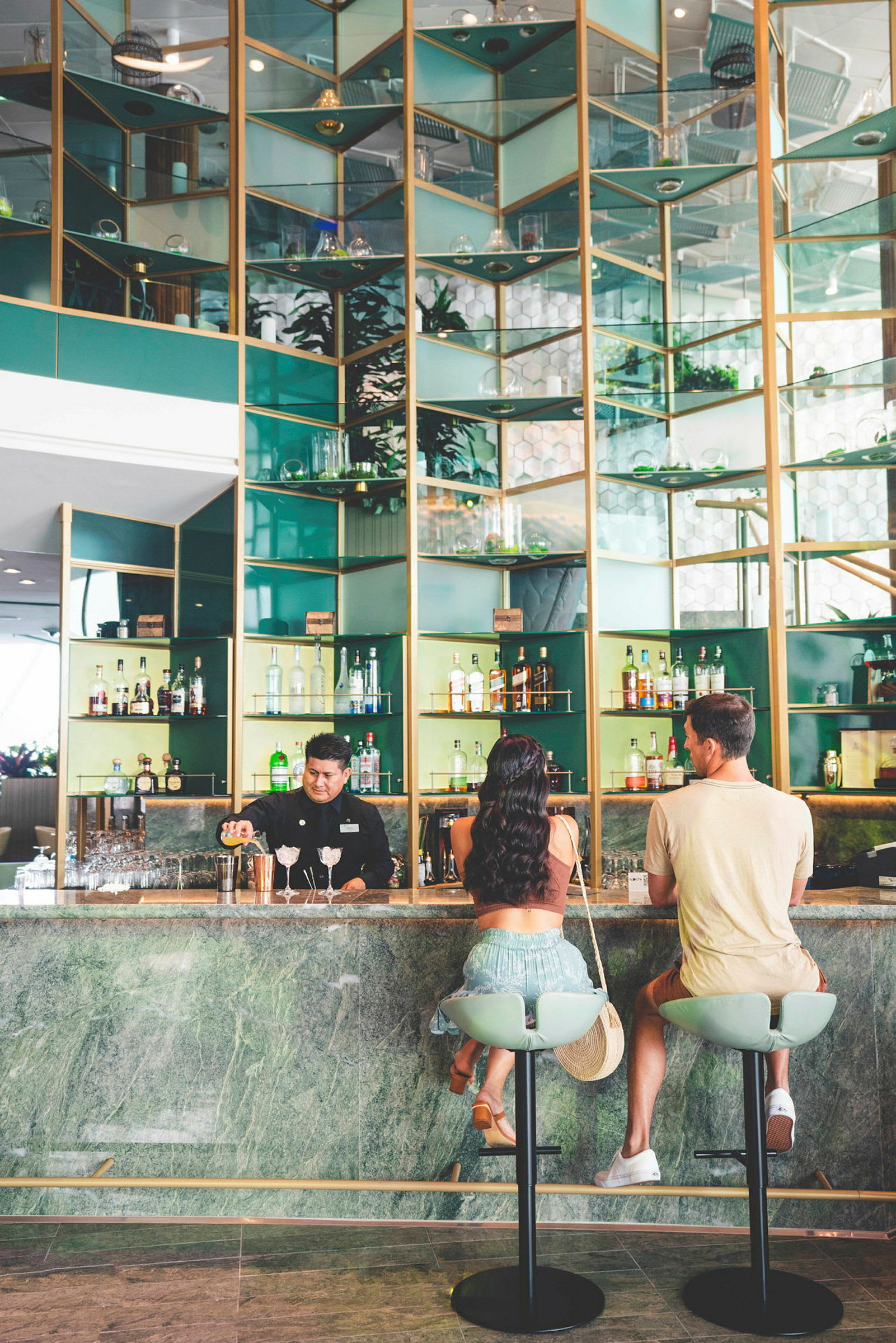En bar med grønne og gylne detaljer, der to personer sitter på barstoler og en person står bak baren. (AI-generert tekst)