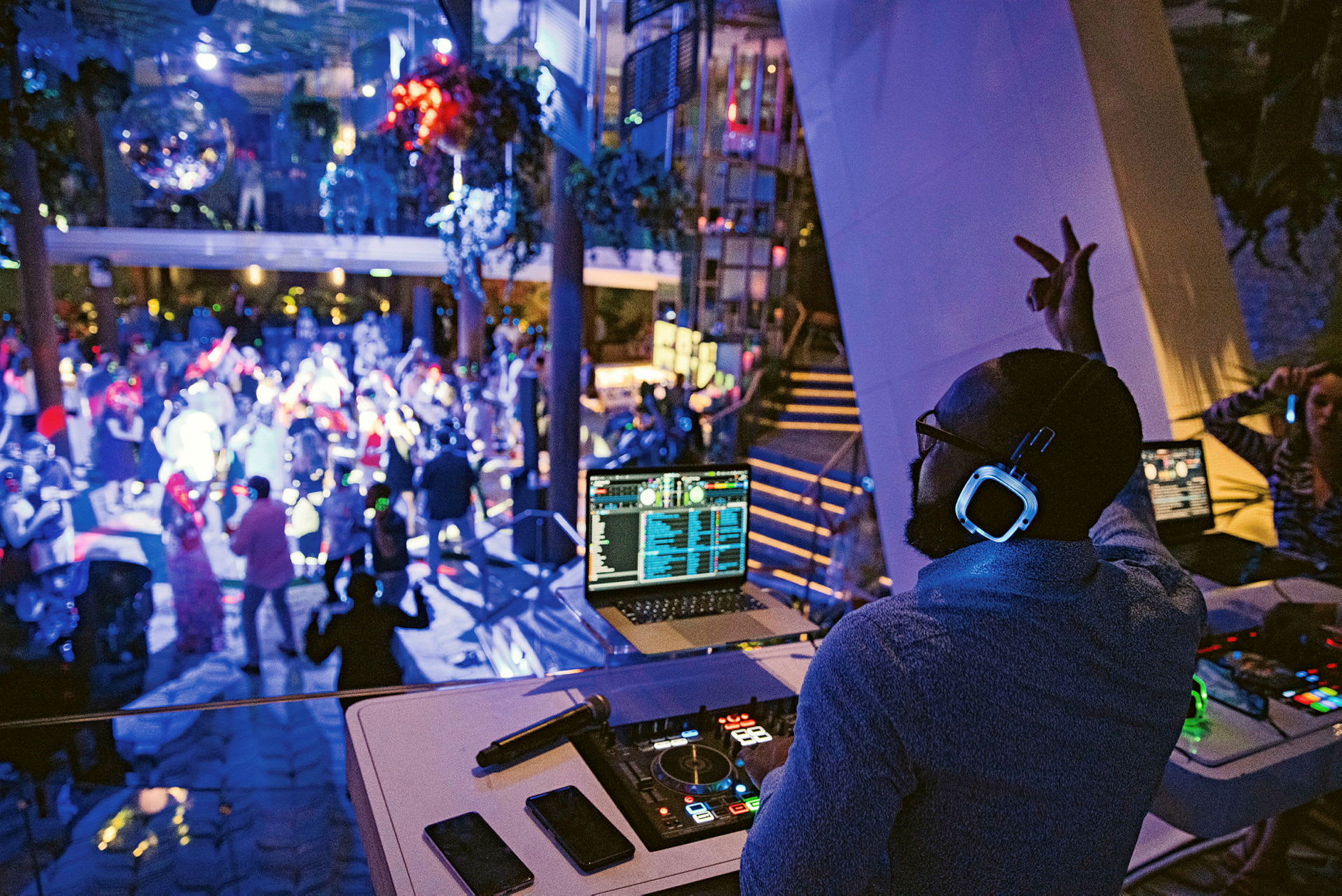 En DJ står ved sitt miksebord og spiller musikk på en nattklubb hvor folk danser under blinkende lys. (AI-generert tekst)