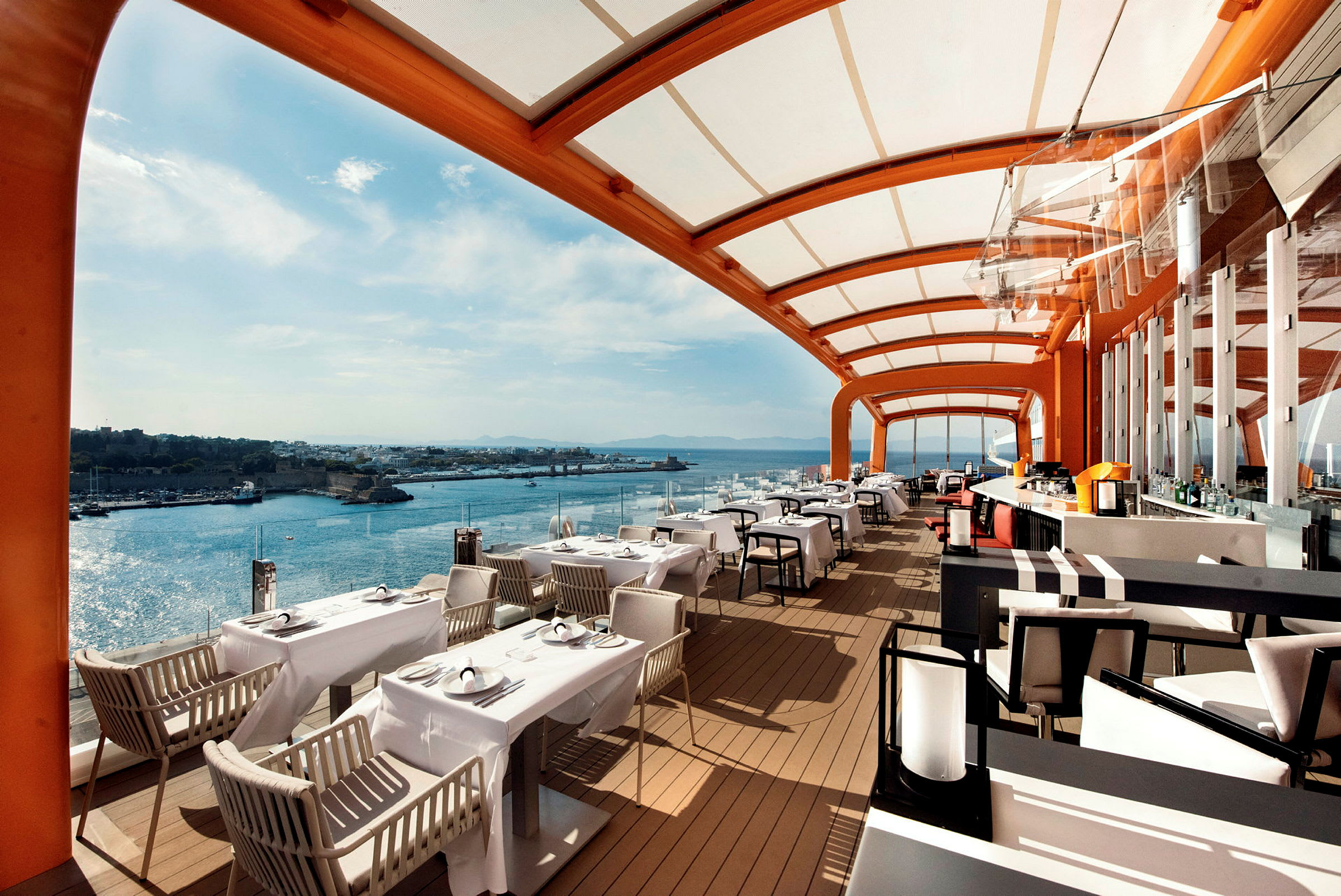 Utsikt over en restaurant med overdekket terrasse og havet i bakgrunnen. (AI-generert tekst)