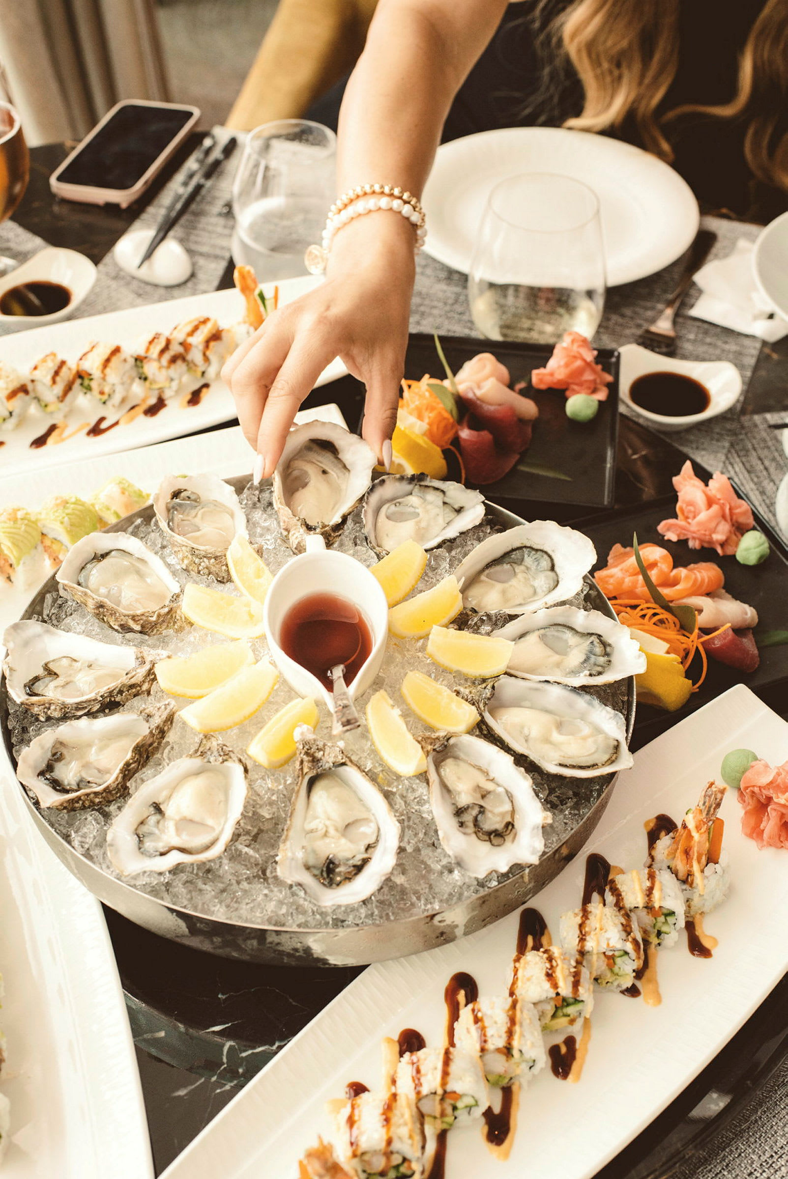En tallerken med østers servert på is med sitronbåter i midten, sammen med sushi og sashimi på andre tallerkener. (AI-generert tekst)