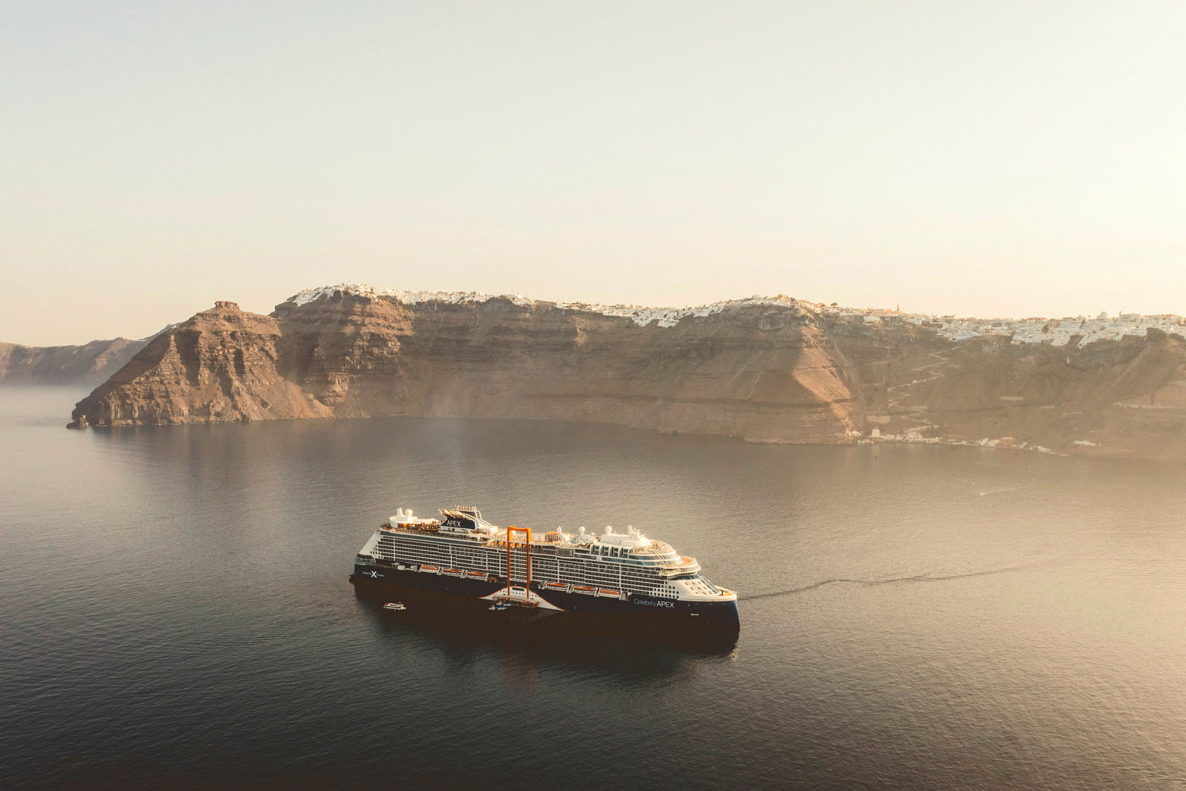 Et cruiseskip ligger ankret i en rolig havbukten med høye klipper i bakgrunnen. (AI-generert tekst)