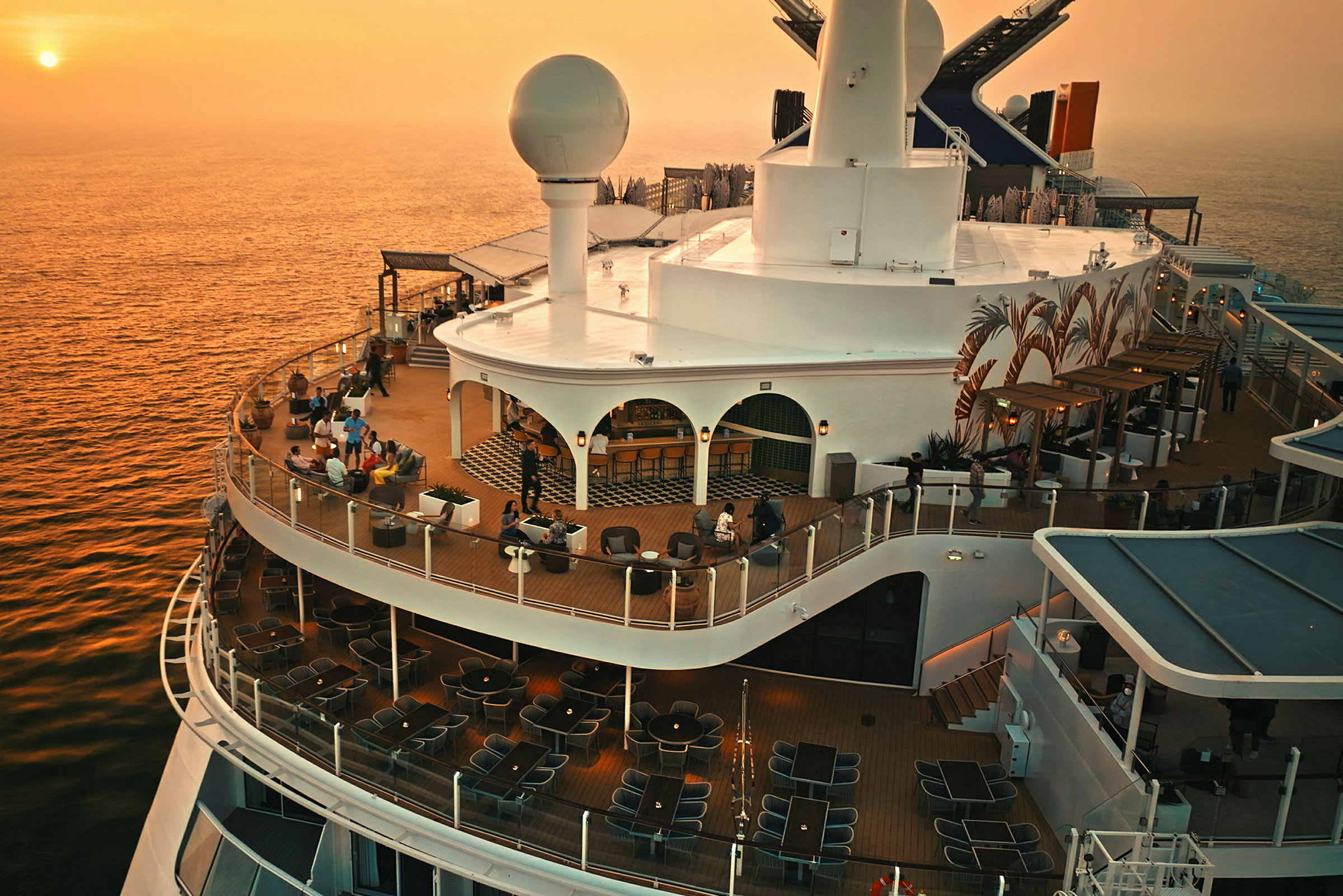 Bilde av dekket på et cruiseskip ved solnedgang med sitteplasser og en bar. (AI-generert tekst)
