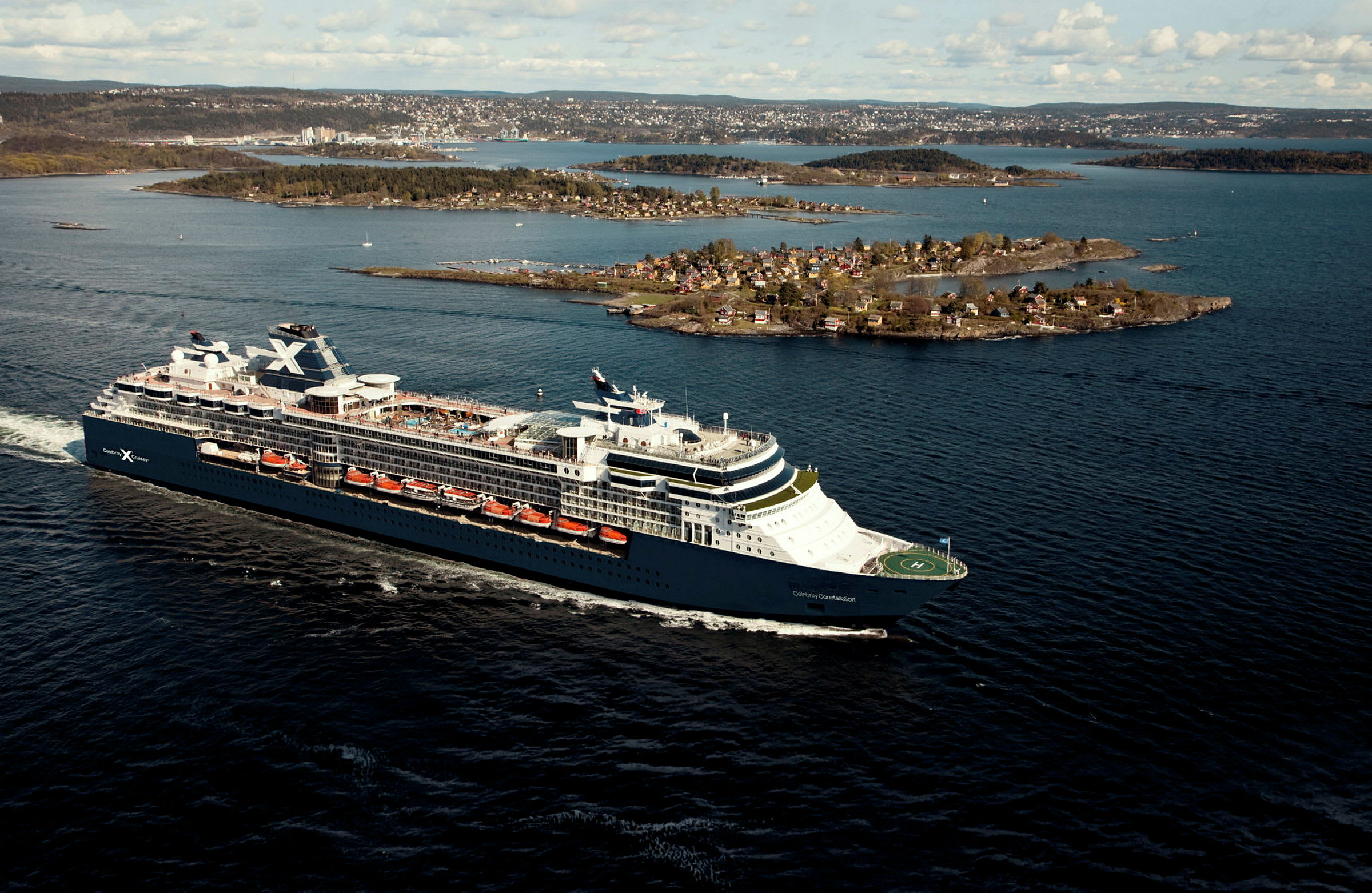 Et cruiseskip seiler på en blå sjø med øyer i bakgrunnen. (AI-generert tekst)