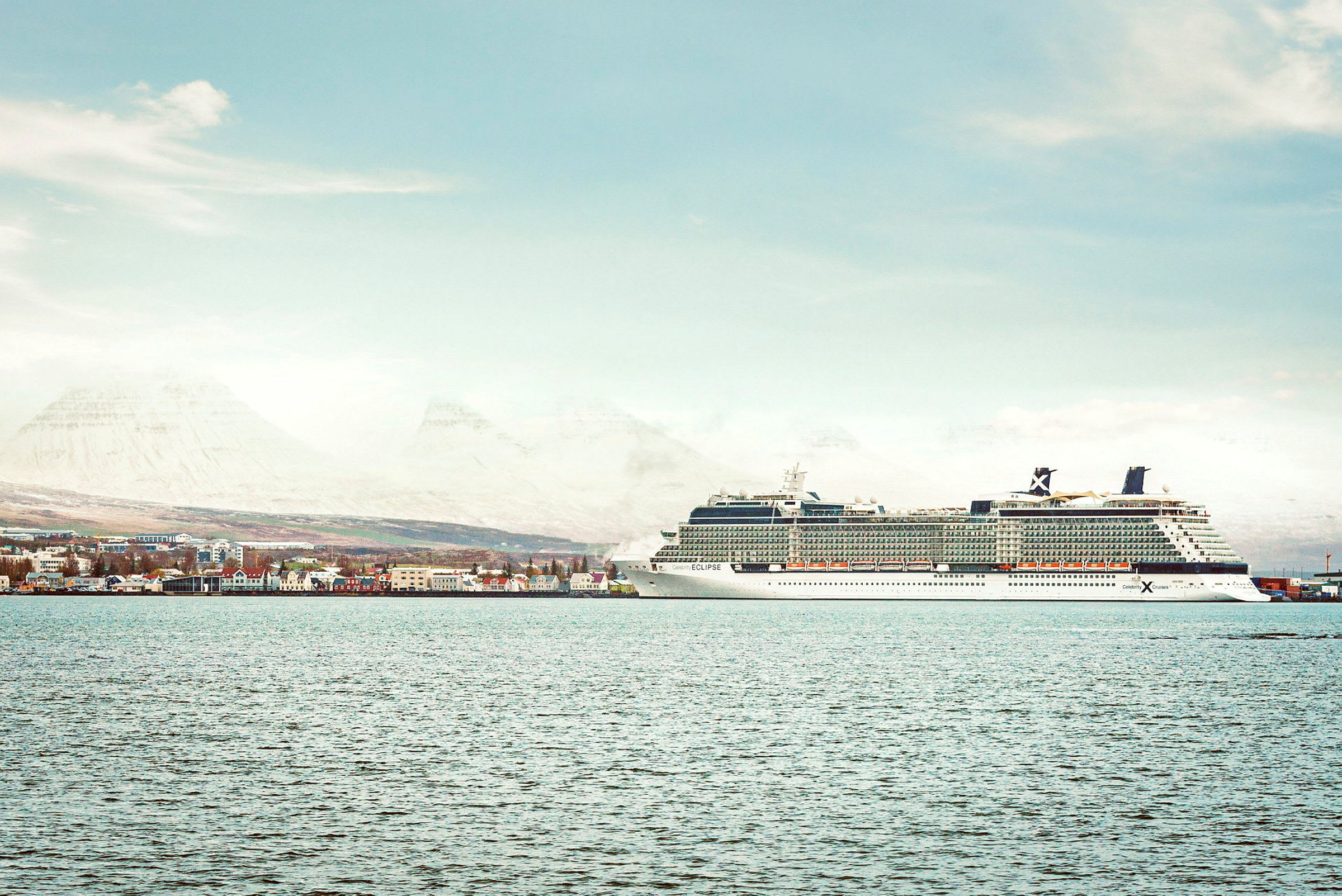 Cruiseskip ved havn, by og fjell i bakgrunnen. (AI-generert tekst)