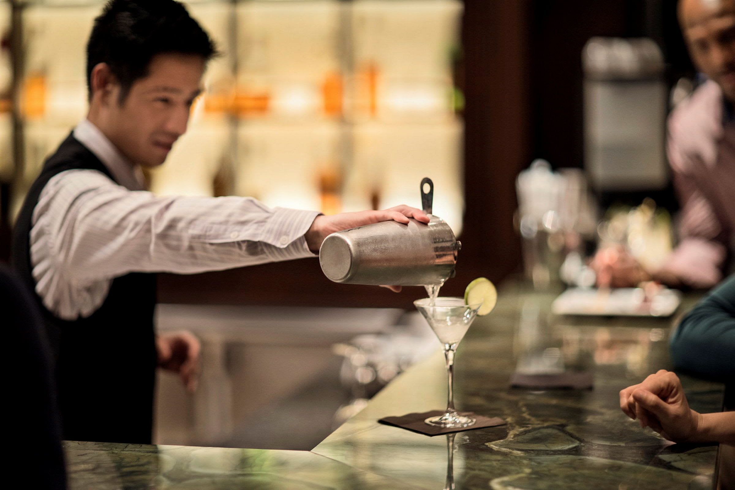 En servitør som heller en drink i et cocktailglass. (AI-generert tekst)