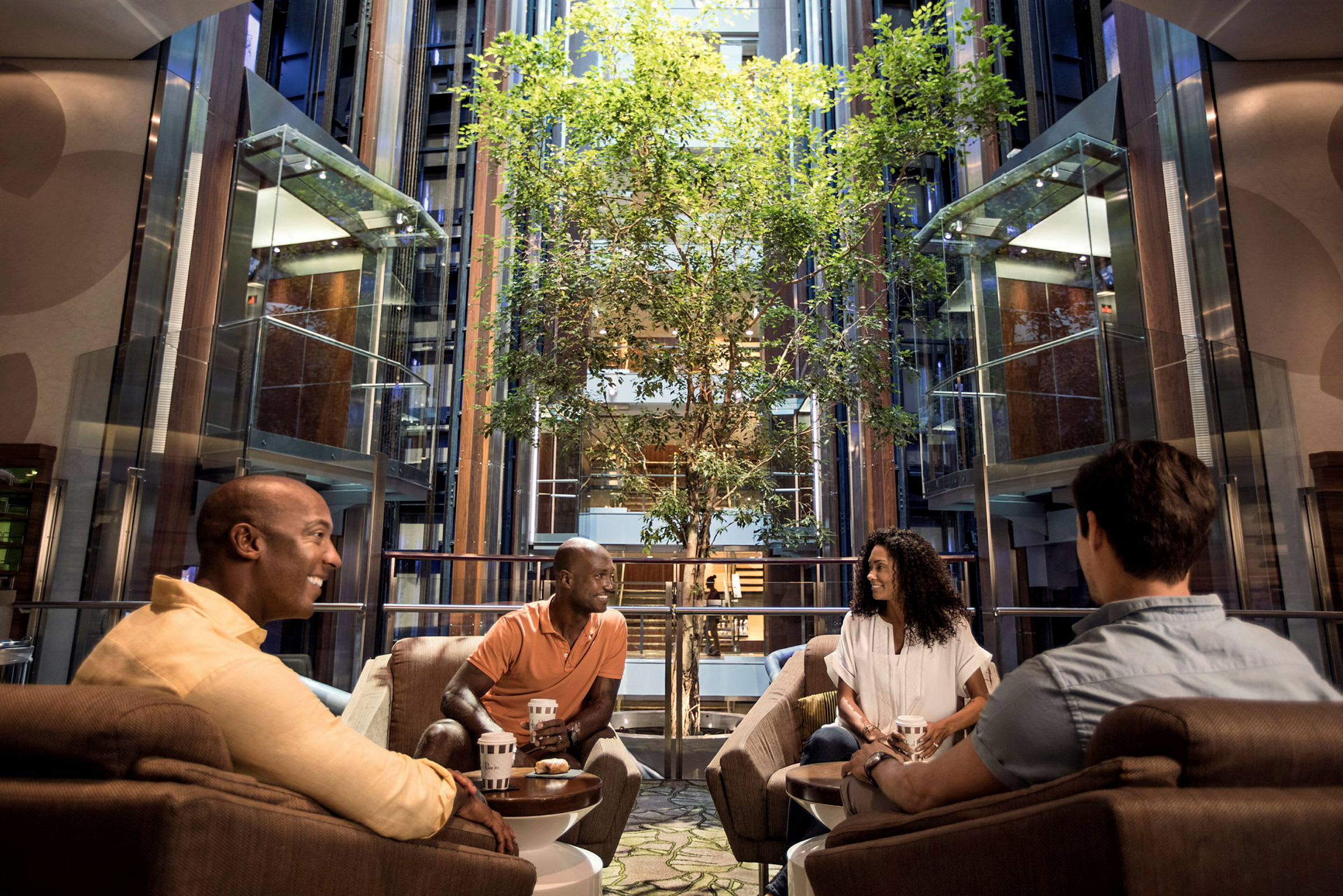 Personer sitter i en moderne hotellobby med et treområde og heiser. (AI-generert tekst)
