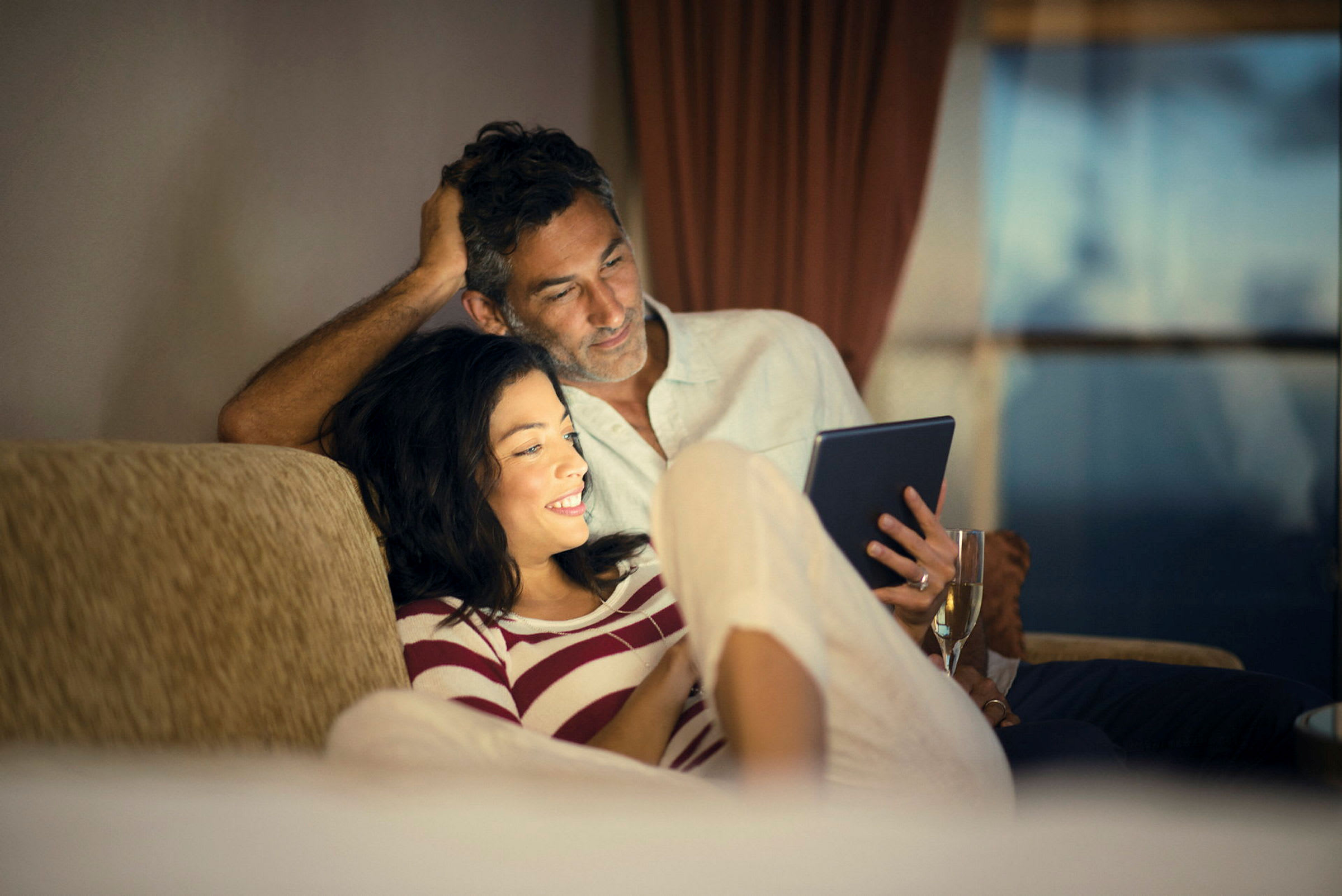 Person holder en nettbrett og et glass på en sofa. (AI-generert tekst)